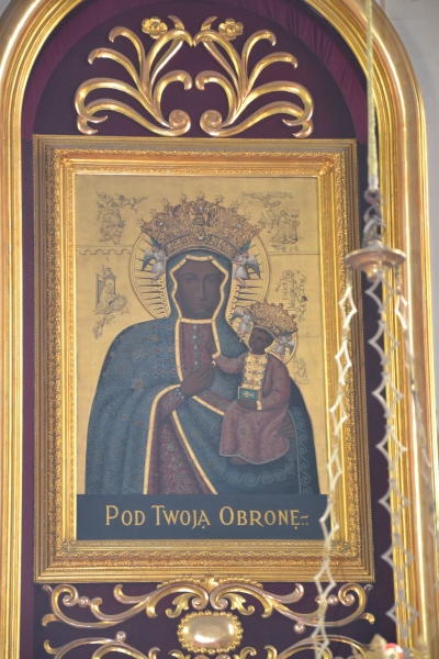 Ikona Matki Boskiej Częstochowskiej z Jezusem, oboje w złotych koronach, w złotej ramie na purpurowym tle z dekoracyjnymi złotymi ornamentami, z napisem "Pod Twoją obronę"