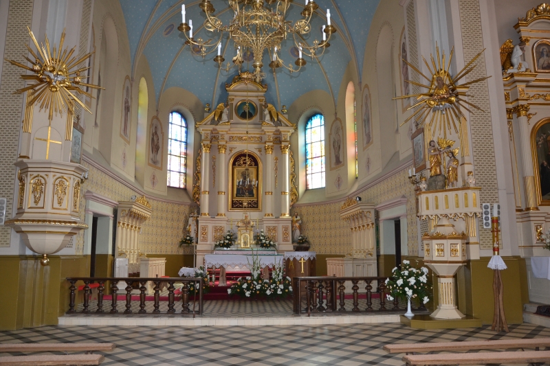 Wnętrze kościoła z ołtarzem zdobionym złotem, kwiatami i obrazem, witrażowe okna, błękitne sklepienie z żyrandolem, marmurowa podłoga w biało-czarne kwadraty.