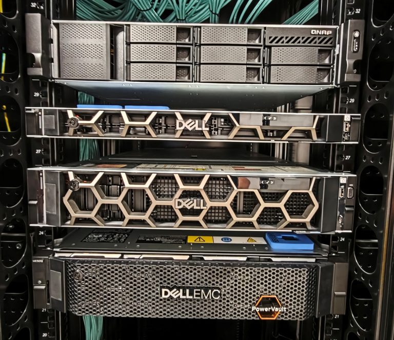 Cztery moduły sprzętowe w szafie serwerowej, trzy z logo Dell, jeden QNAP, przewody sieciowe w tle.