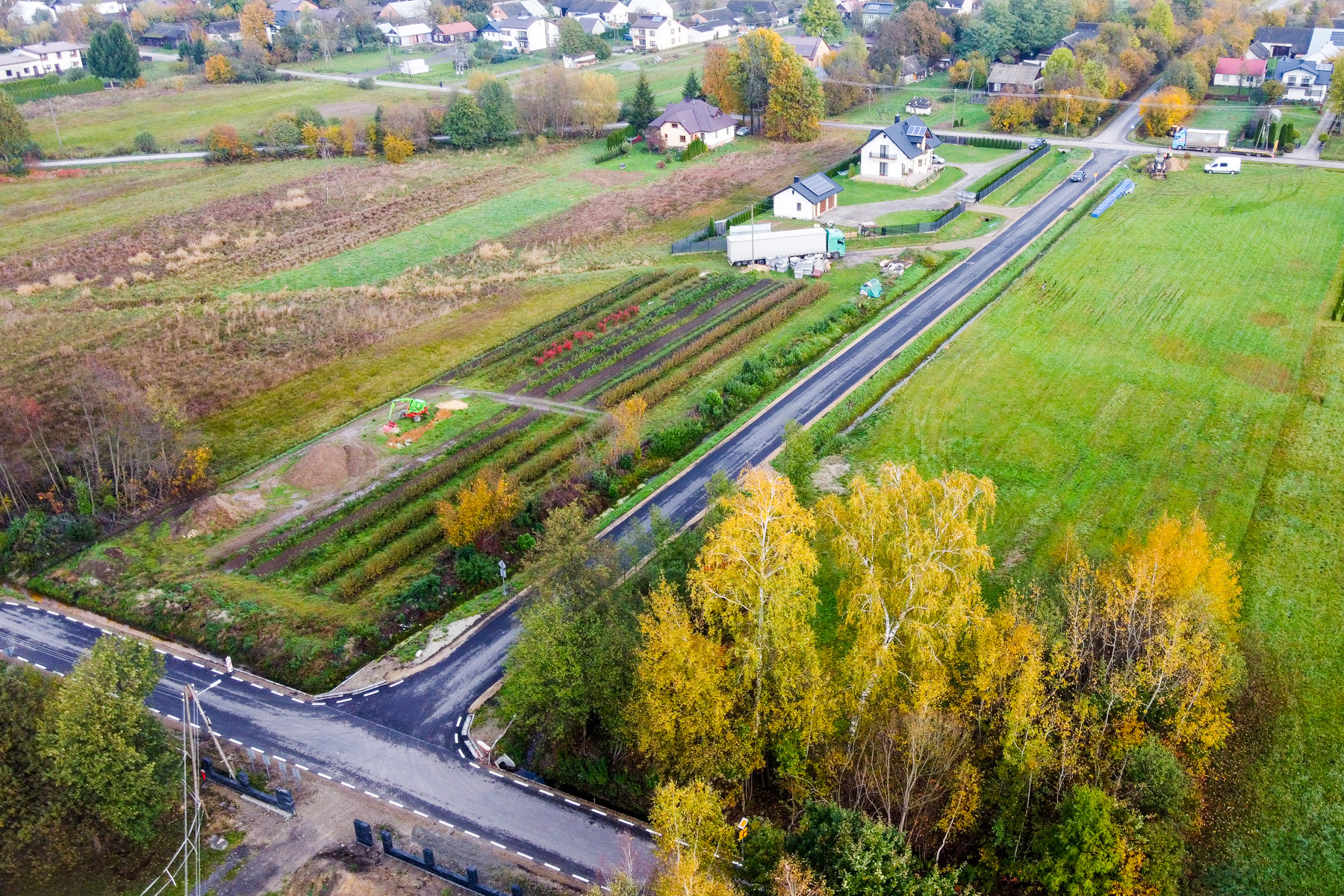 Widok z lotu ptaka na wiejską drogę, pola uprawne, domy i drzewa z żółtymi liśćmi jesienią.