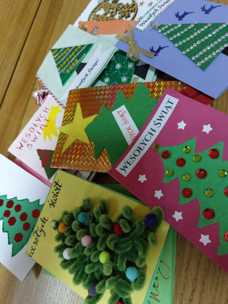 Ręcznie wykonane kartki świąteczne z motywem choinek, gwiazd i napisem "Wesołych Świąt", różne kolory i ozdoby, ułożone na drewnianej powierzchni.
