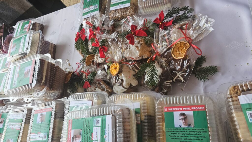 Paczki z ciastkami i piernikami, dekorowane gałązkami iglastymi, czerwonymi kokardami i suszonymi plasterkami pomarańczy, na białym obrusie.